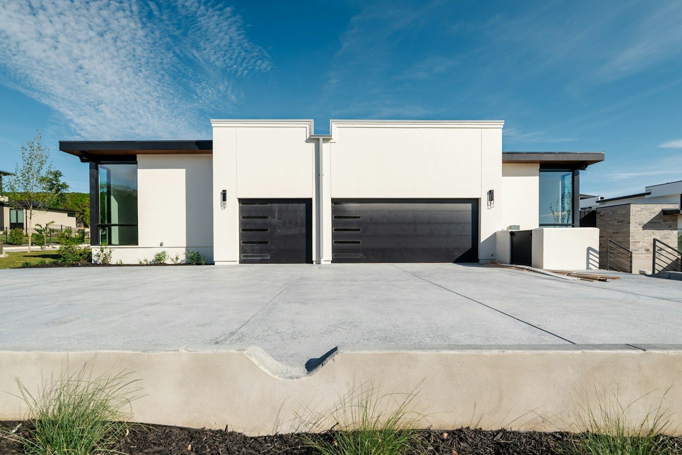 Modern white home with a wide concrete driveway under blue sky